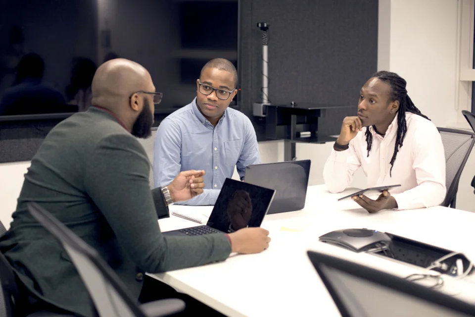 Three colleagues discussing work around a table with laptops and a tablet